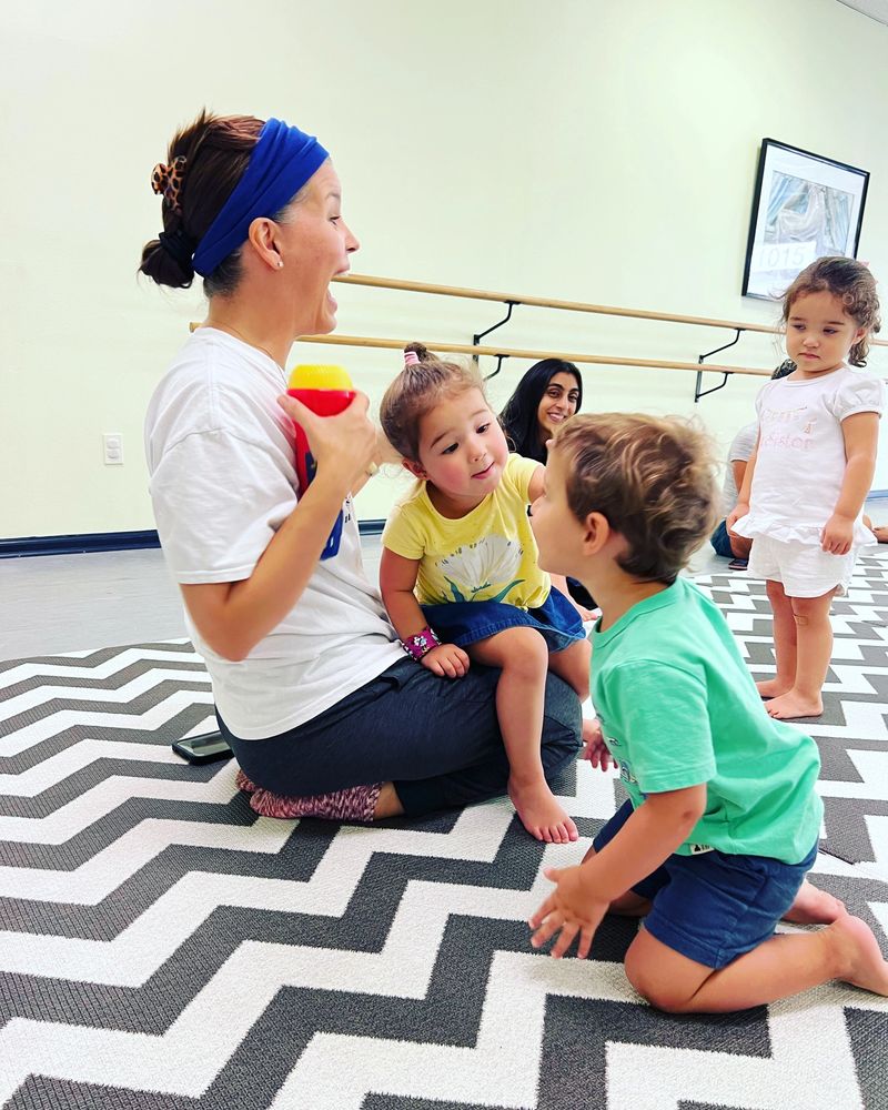 A woman and children engage in a playful, joyful moment on a zigzag patterned floor.