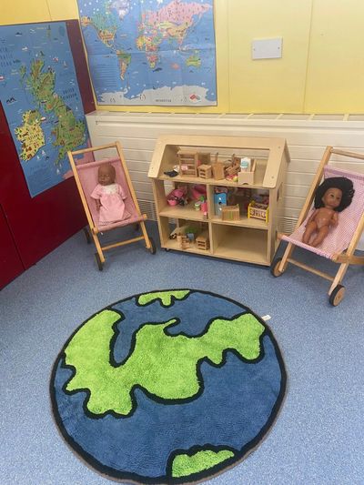 Children's play area with dolls, a dollhouse, and a world map rug.