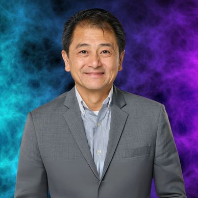 Man in a gray suit smiling against a blue and purple smoky backdrop.