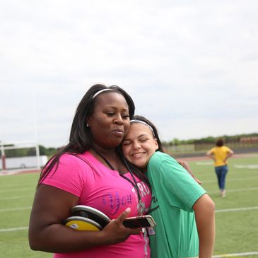 Two women sharing a warm hug on a sports field.