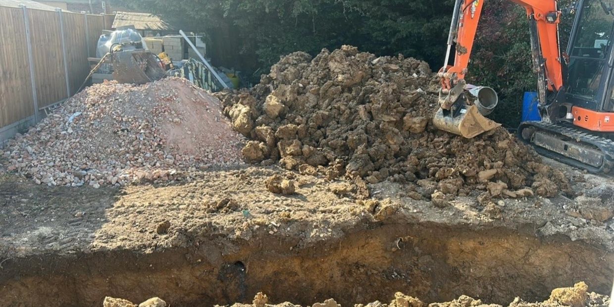 Excavator digging soil and two large dirt piles in a backyard construction site.