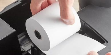 Hands loading a thermal paper roll into a receipt printer.