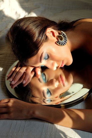 Woman with blue eyeshadow resting face on a mirror, showing a reflective portrait.