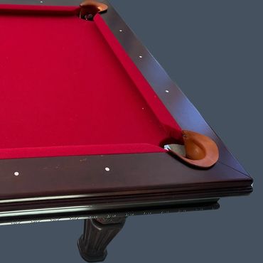Close-up of a red felt pool table corner with wooden pocket and ornate leg.