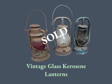 Three vintage glass kerosene lanterns with metal frames and handles.