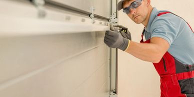 Garage door installation: worker aligns large sectional door on tracks with tools.

