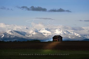 granary lit by a shaft of light with snow covered mountains in the background
