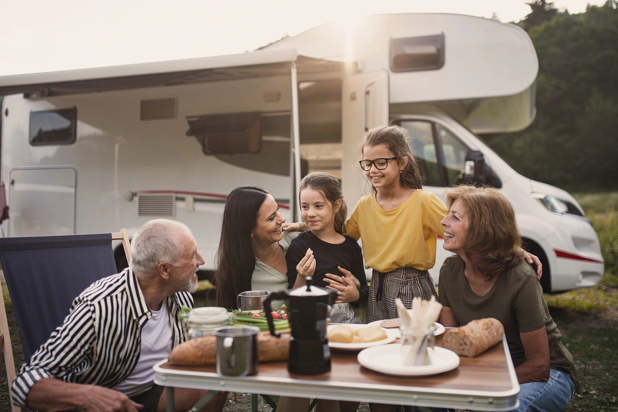 family of five having a meakl and conversation outside with their RV or motorhome behind them