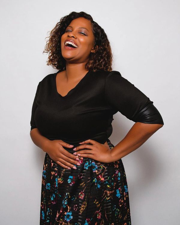 A joyful woman laughing with hands on her waist, wearing a black top and colorful skirt.