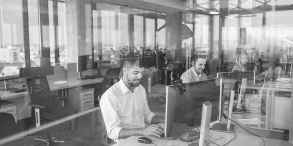 People working at computers in a modern office with glass walls.