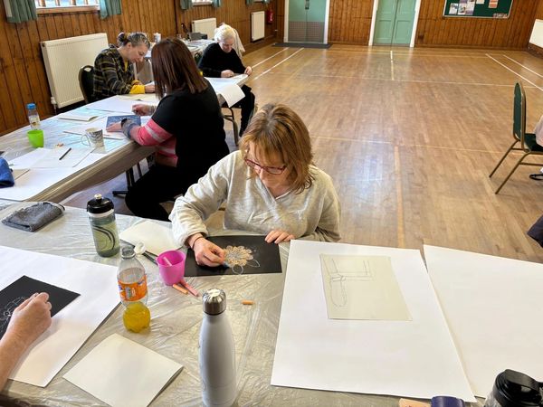 People drawing and coloring at a table in a hall.