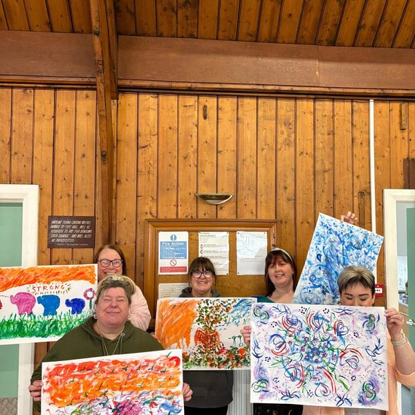 A group of five women holding colorful paintings indoors.