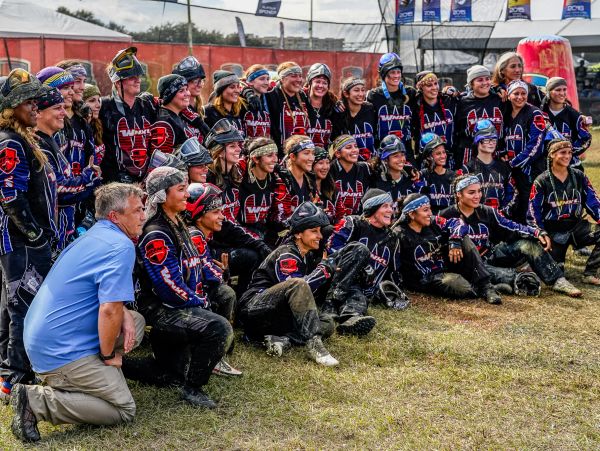 Large group of paintball players in gear posing for a photo on grass.