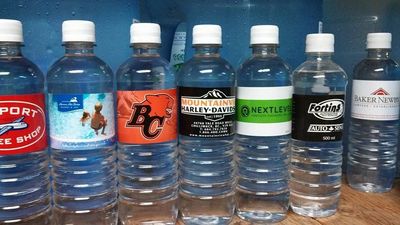 Six water bottles with different labels lined up on a table.