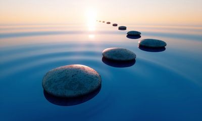Smooth stones form a path across calm water at sunset.