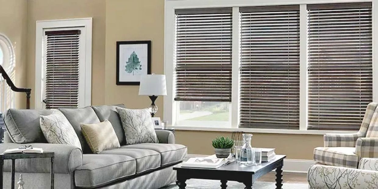 Elegant living room with gray couch and wooden blinds.