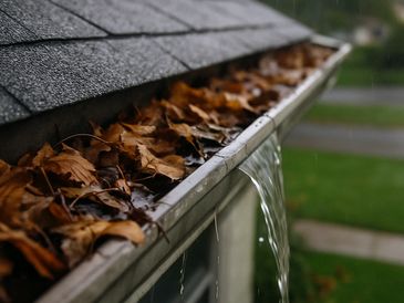 Clogged gutter overflowing with rainwater due to leaves and debris buildup on a residential roof.
