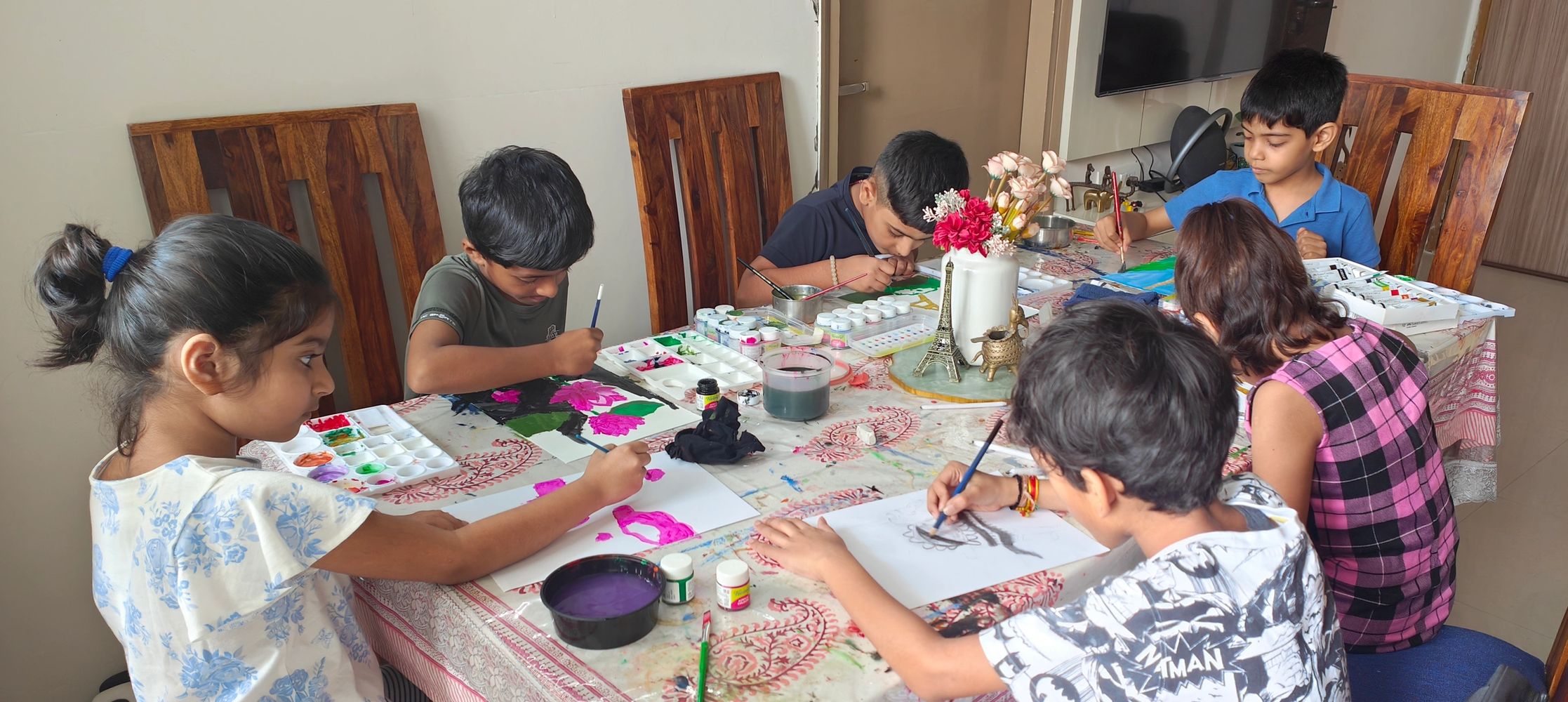 Group of children focused on painting at a table filled with art supplies.