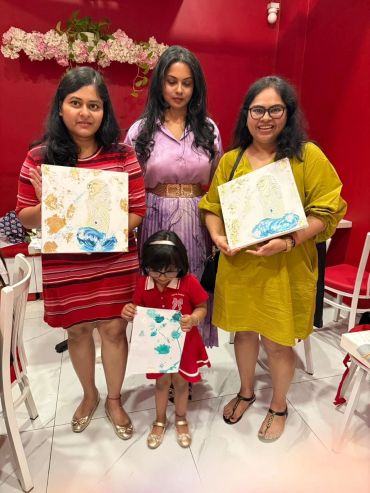 Group photo with three women and a child holding paintings.