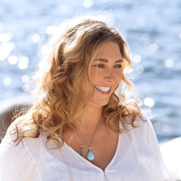 A smiling woman in a white blouse with a sun-shimmering lake in the background