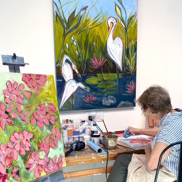 Artist painting in studio with floral and bird artwork.