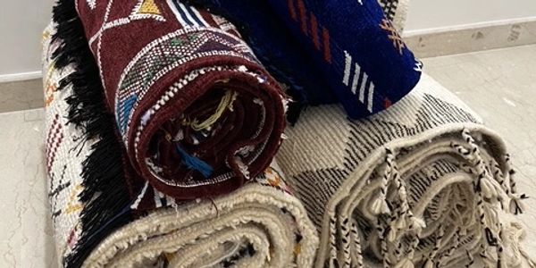 Rolled-up traditional woven rugs with colorful patterns on a floor.