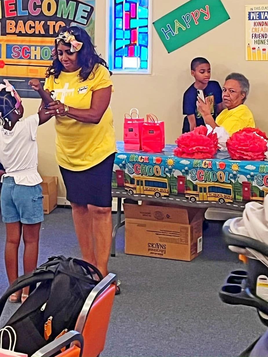 Children and adults celebrate a back-to-school event indoors with decorations and gifts.