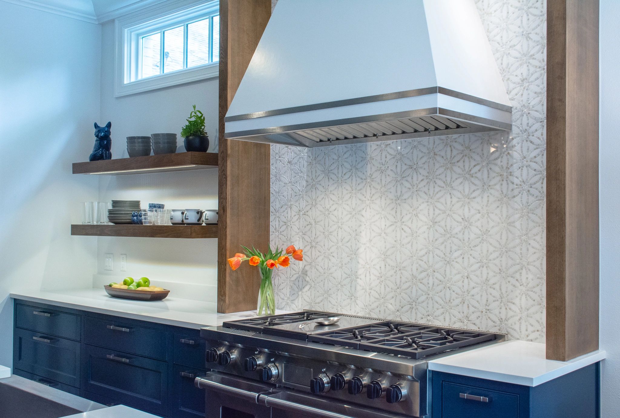 Navy kitchen with floating wood shelves, custom range hood and mosaic backsplash tile in Austin, TX