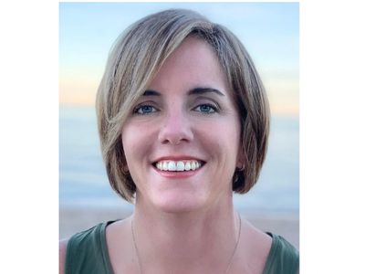 Smiling white woman with a beach and ocean behind her. 