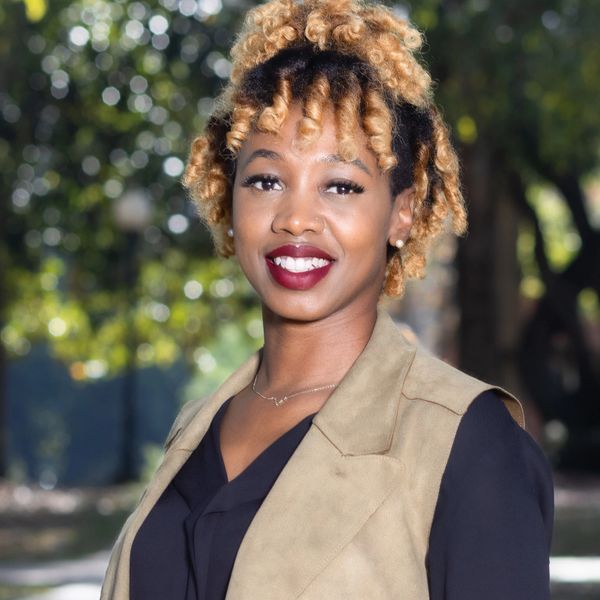 Smiling woman with curly hair poses outdoors in professional attire.