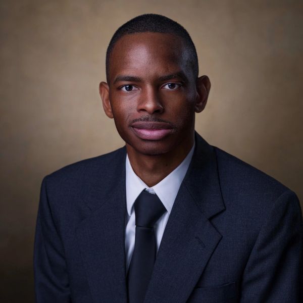 Young man in a dark suit and tie posing for a professional portrait.