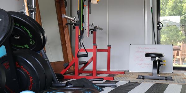Home gym with weights, exercise equipment, and a bench near a whiteboard.