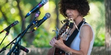 Musician playing guitar and harmonica with microphones.