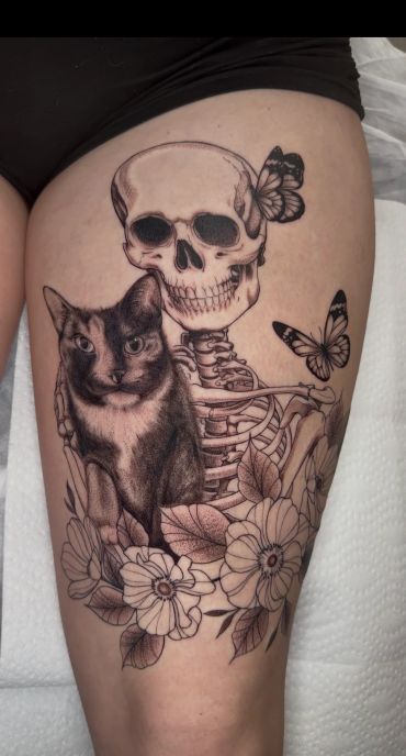 Black and white tattoo of a skeleton, cat, butterflies, and flowers.