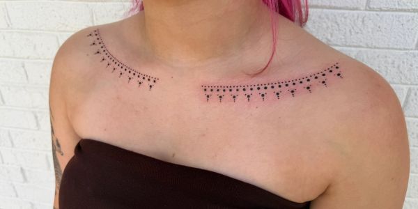 Delicate dot and line patterned tattoo across the upper chest near the collarbone.