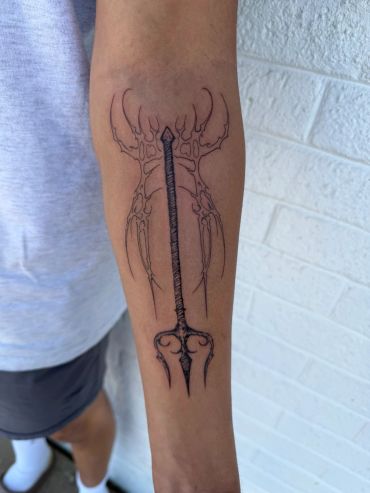 Tattoo of a trident and skeletal design on forearm.