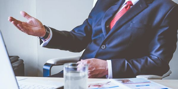 Businessman in suit gesturing during a meeting at his desk.