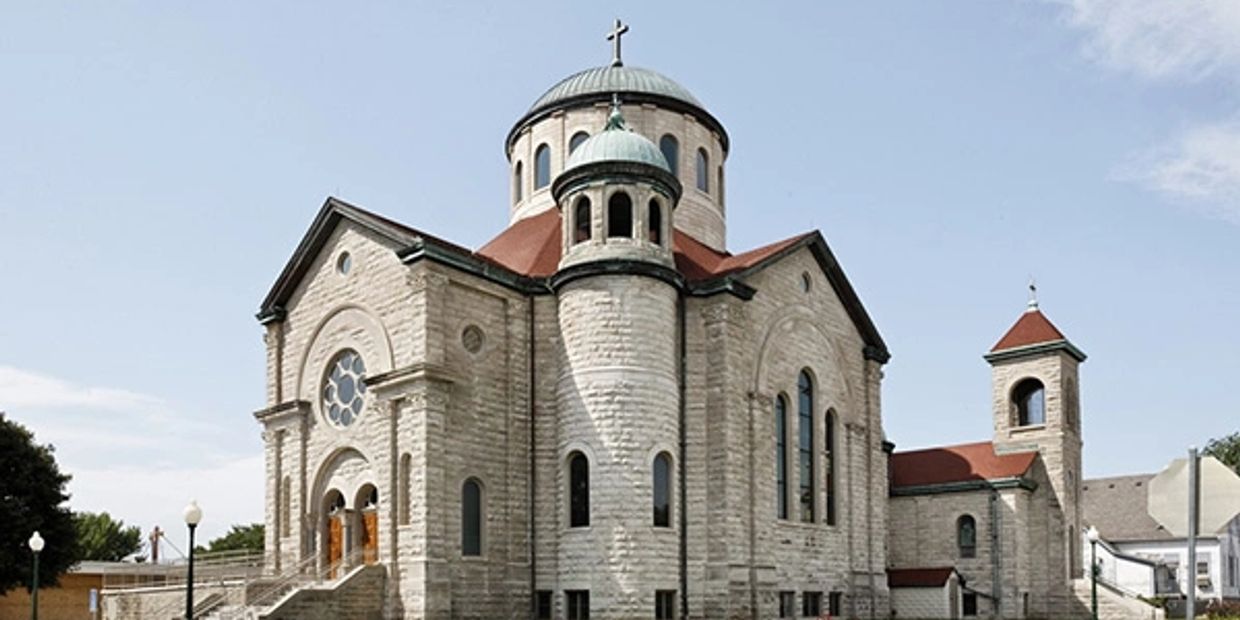 Historic stone church with domed roof and red accents under a clear sky.