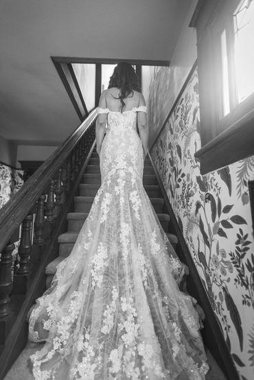 Bride in elegant lace gown ascending stairs in vintage setting.