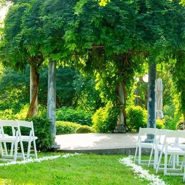 Outdoor wedding setup with white chairs and green vine-covered pergola.