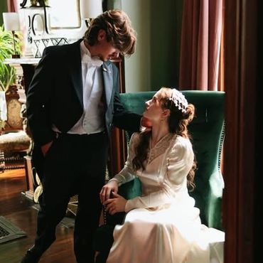 A groom in tuxedo gazes lovingly at bride in vintage wedding dress.