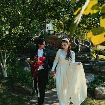 A couple in wedding attire walking hand in hand outdoors on a sunny day.