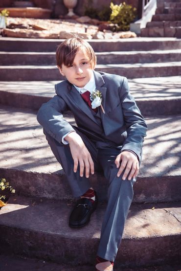 A young boy in a suit sitting on outdoor stone steps.