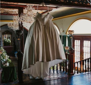 Elegant wedding dress hanging in a vintage room with chandeliers.
