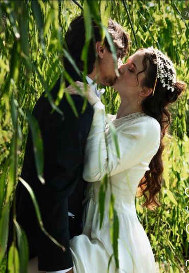 A couple shares a romantic kiss under lush green foliage.