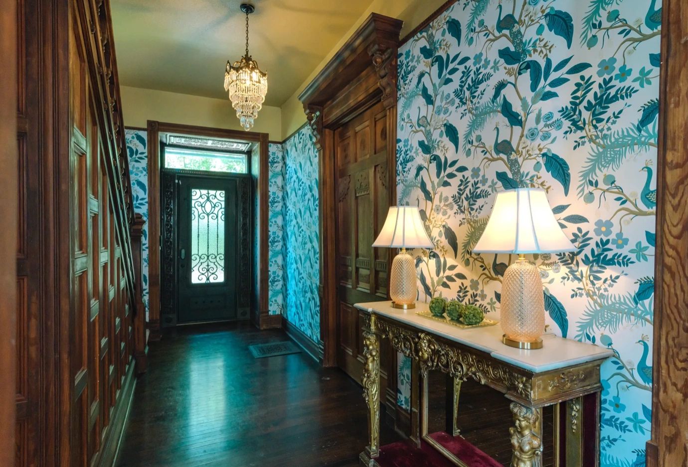 Elegant hallway with ornate wooden door, floral wallpaper, and decorative lamps.