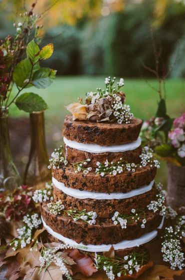 Three-tiered rustic cake decorated with white flowers and greenery.