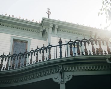 A vintage balcony with ornate iron railing on a white building.