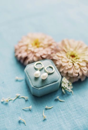 Elegant pearl earrings on a blue velvet box with soft pink flowers.