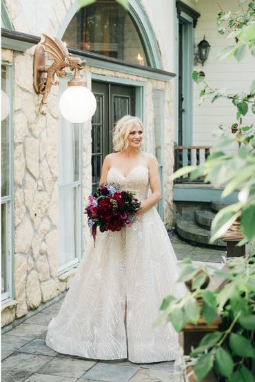 Bride in elegant white gown holding a bouquet of dark red flowers.